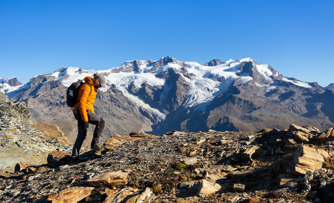 A hiker explores rocky trails in Staffal, Aosta Valley, with snow-capped Alps in the background.